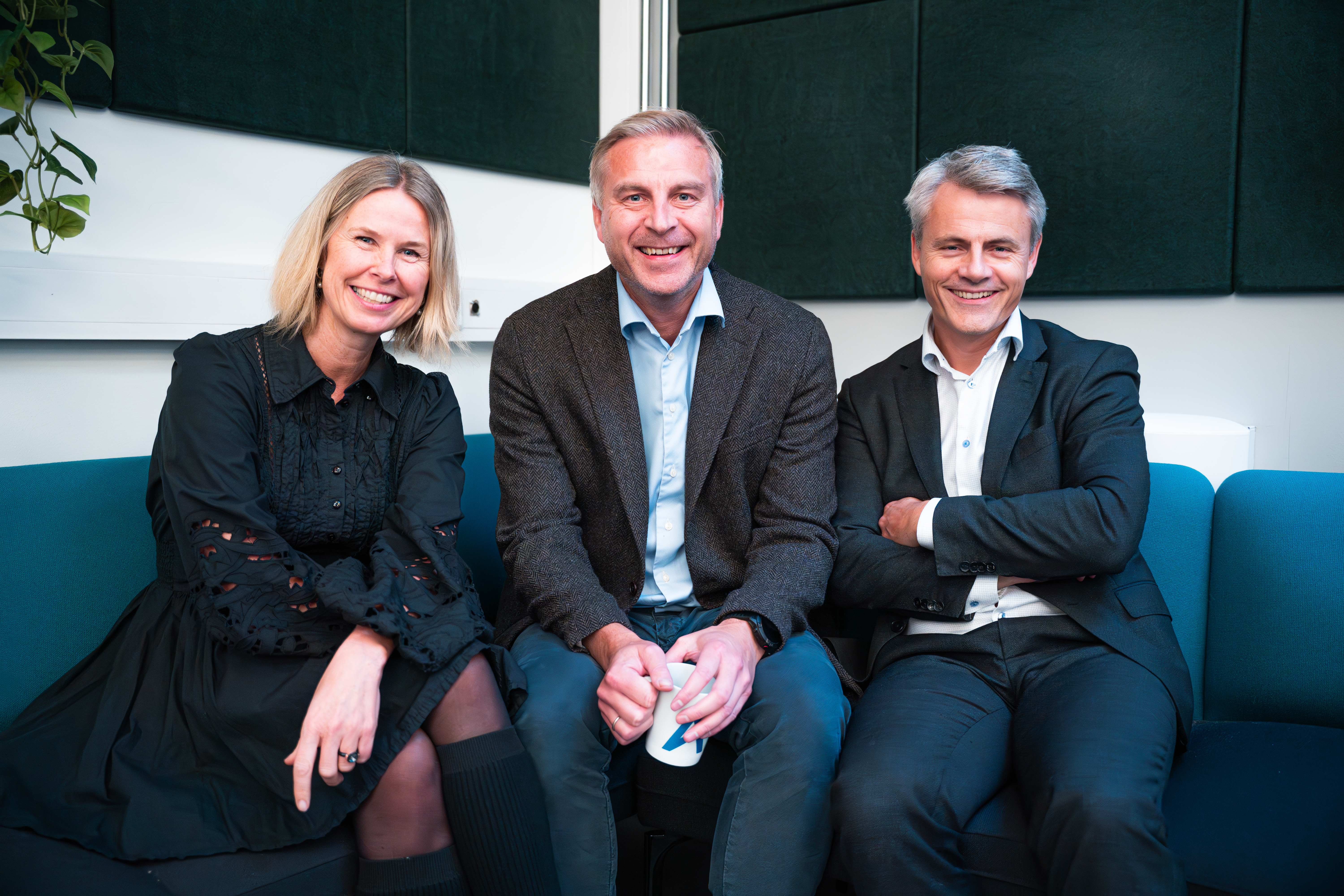 3 personer sitter i en sofa og smiler til kamera