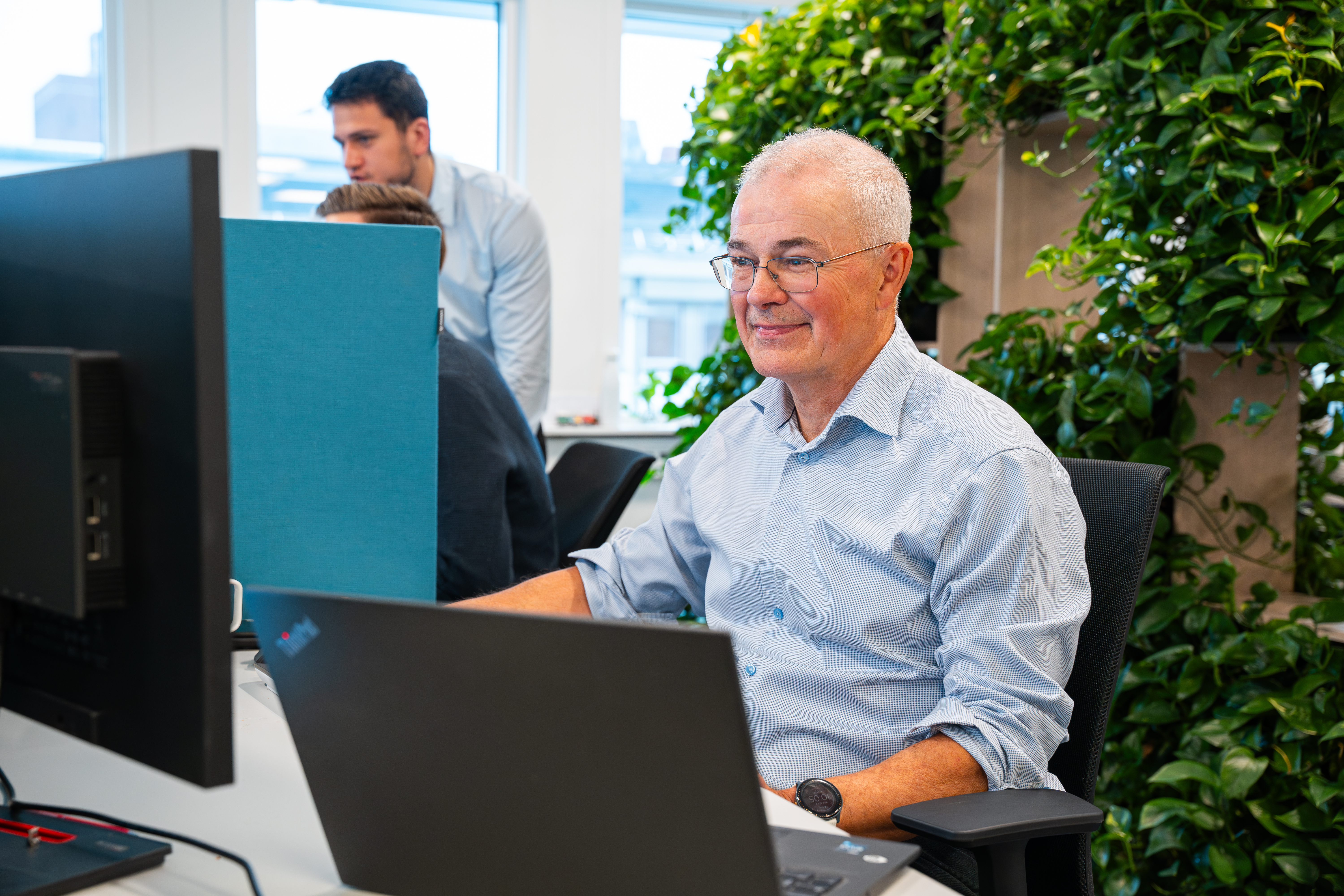 Mann jobber på pc, bak står en plante-dekorasjon