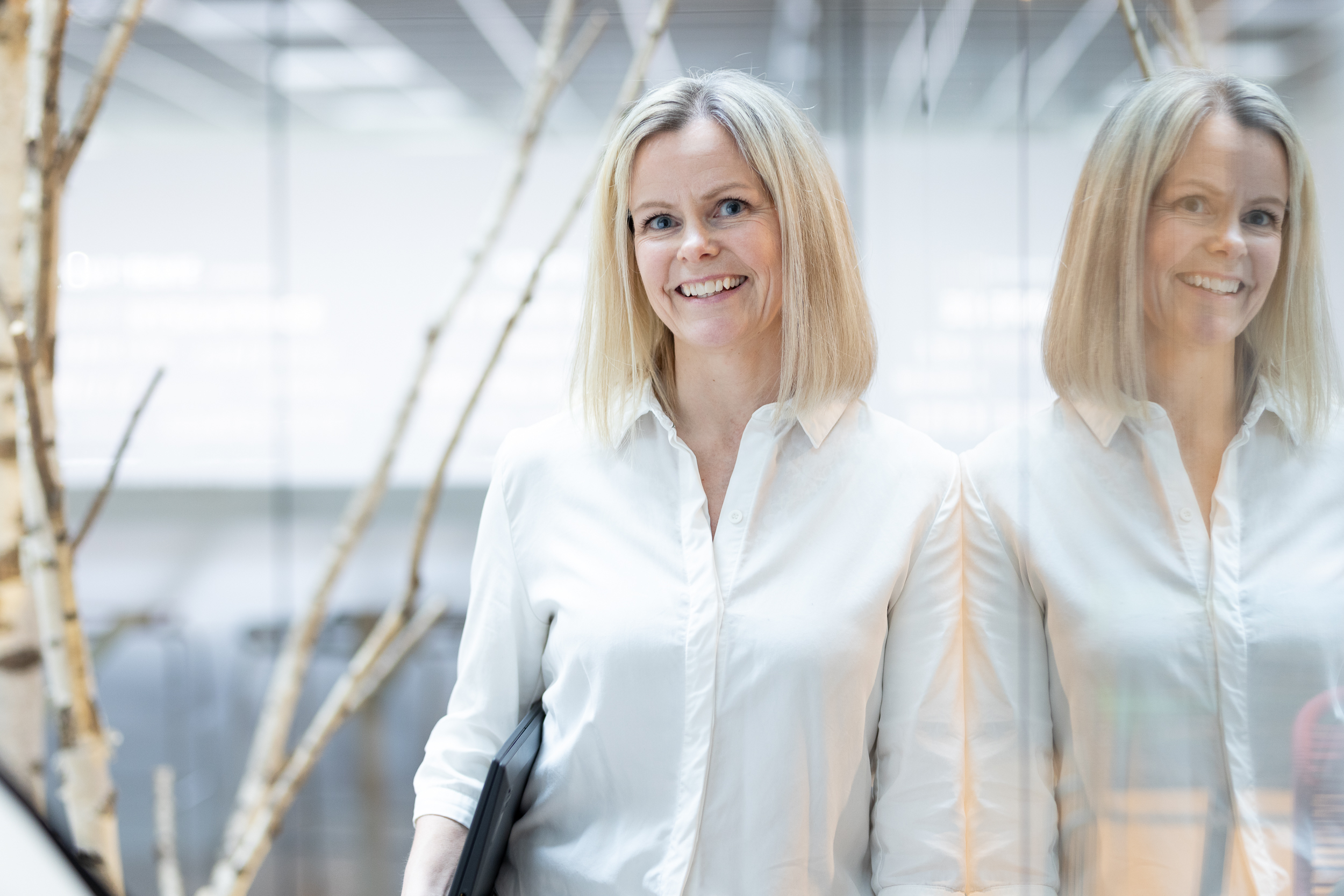 Dame som smiler ved siden av et reflekterende glassvegg