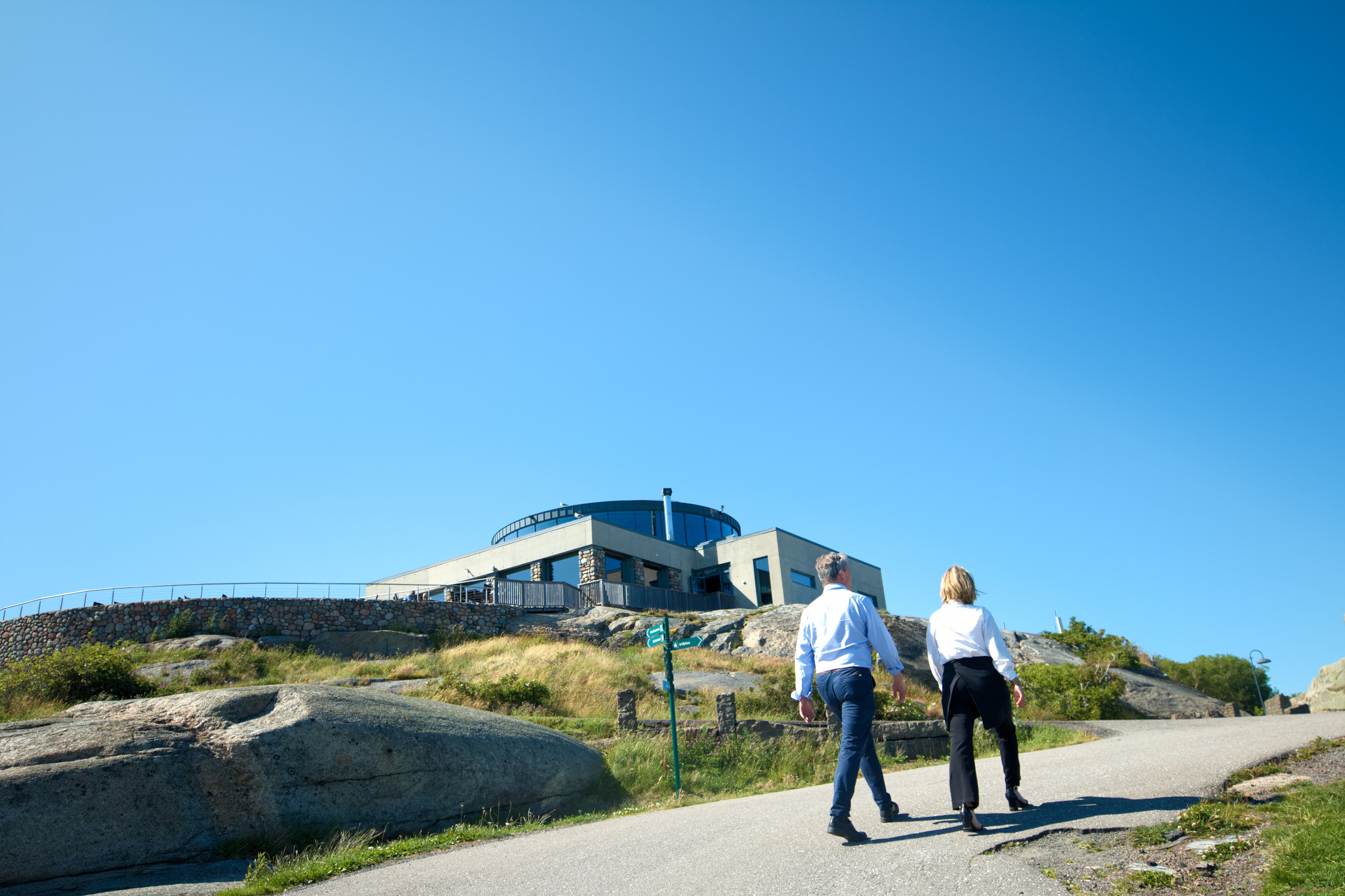 To ansatte utenfor Verdens Ende Spiseriet på en solrik dag med hav og arkitektur i bakgrunnen