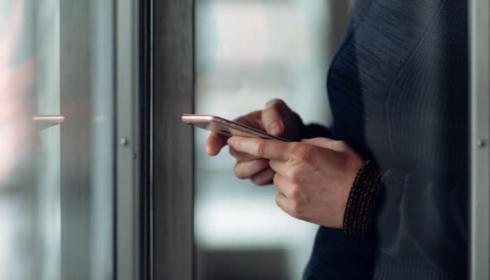 Kvinne taster på mobil ved et vindu